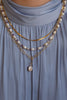 Image of three layered necklaces displayed on a light blue collared dress. The top necklace is a sleek herringbone chain, followed by a handcrafted beaded necklace adorned with freshwater pearls, amethyst, and rose quartz. The third necklace features a string of pearls on an elongated oval chain, adding a classic touch to the ensemble. Each piece complements the others, creating a harmonious and stylish look.