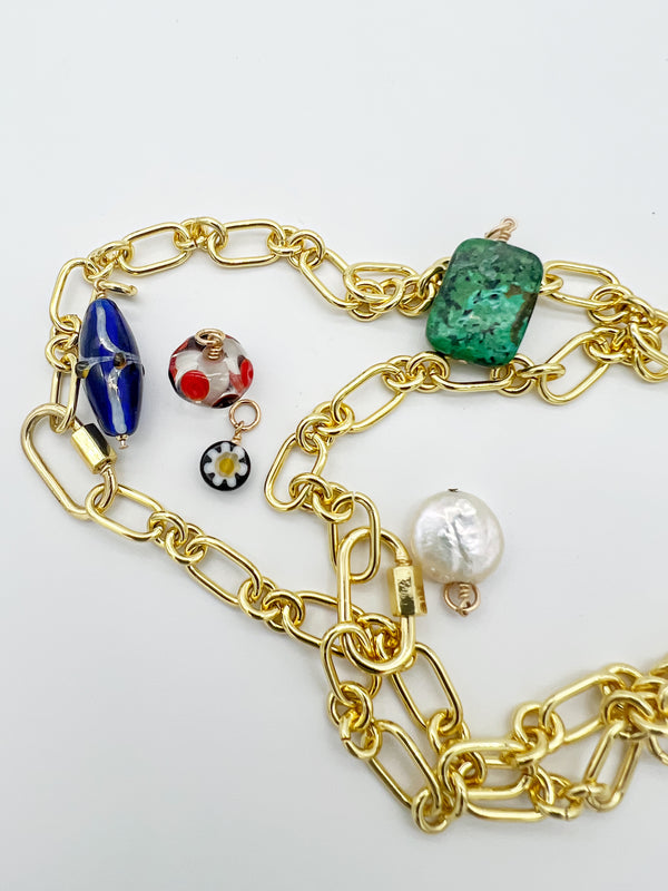 Golden link 14k gold-filled necklace styled with multiple charms including a blue glass bead, red dot glass bead, flower bead, malachite charm, flat coin pearl, and screw carabiner links, displayed on a white background.