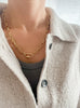 Golden Link necklace with alternating long and short links, worn by a model over an open button-up collared sweater and gray tank top, showing how it drapes naturally.
