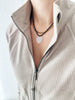 Opalite heart pendant on a black leather cord layered with a gold necklace, worn by a model in a textured zip-up collar sweater