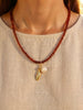 Red beaded carnelian necklace with a 14k gold-filled fish charm and a freshwater pearl charm at the centre, shown on a model wearing a beige sand top.