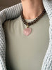 12 mm round smoky quartz strand necklace with a carabiner push clasp and rose quartz heart charm, worn by a model in a light green T-shirt and light blue sweater draped over her shoulders.