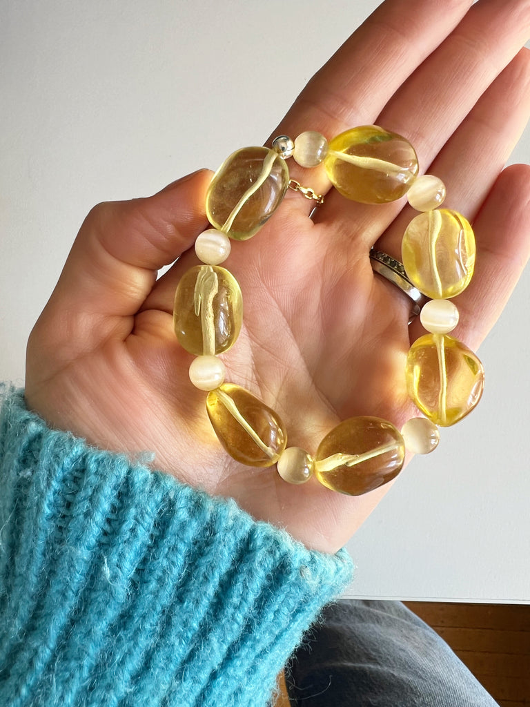 Yellow citrine beaded bracelet with pale yellow glass beads held in a hand.