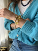 Yellow citrine beaded bracelet stacked with a gold bangle, worn on a wrist with a turquoise cardigan and jeans.